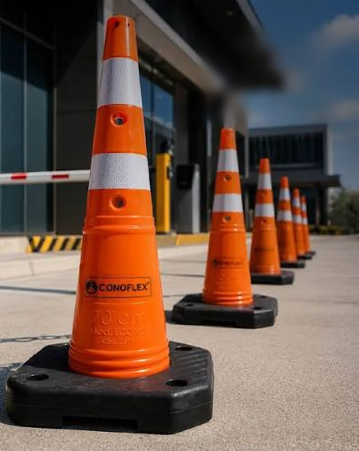 Fila de conos de señalización naranjas Conoflex con bandas reflectivas frente a un edificio