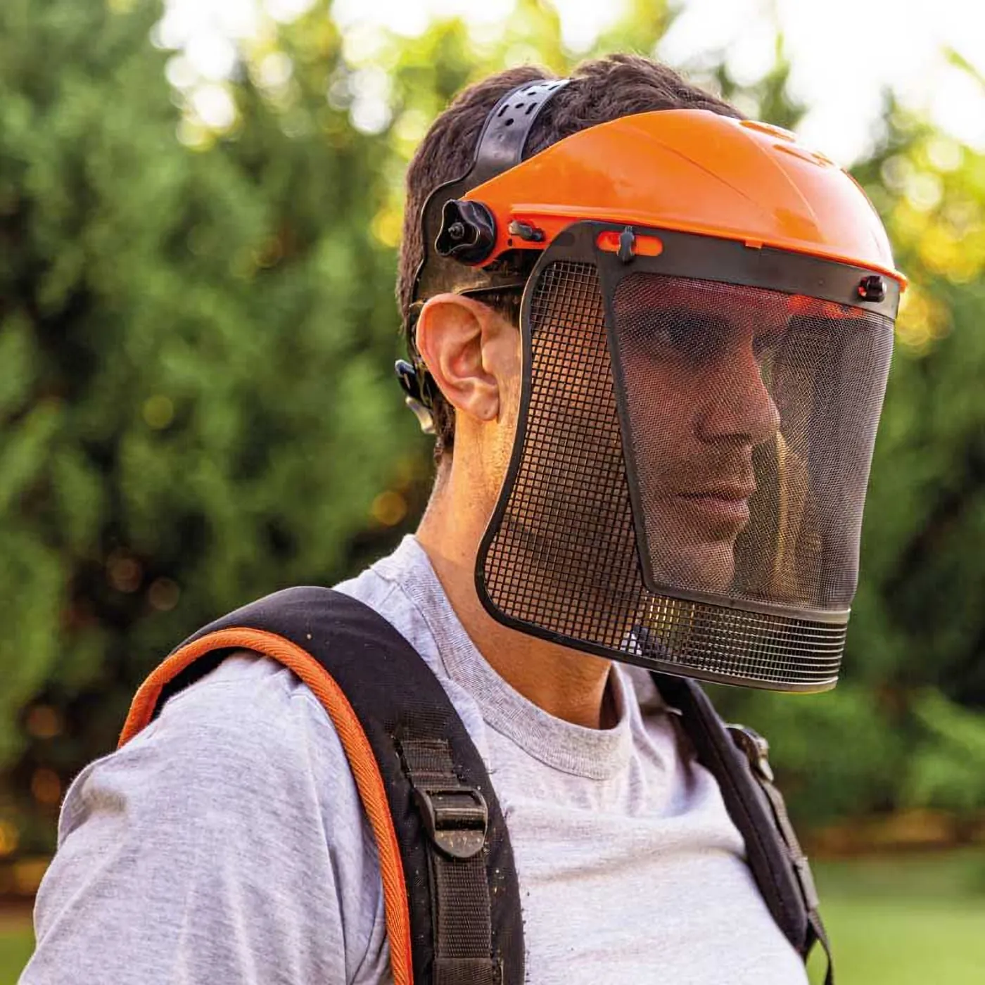 Trabajador con casco porta visor naranja y malla facial Libus del kit desmalezador, al aire libre
